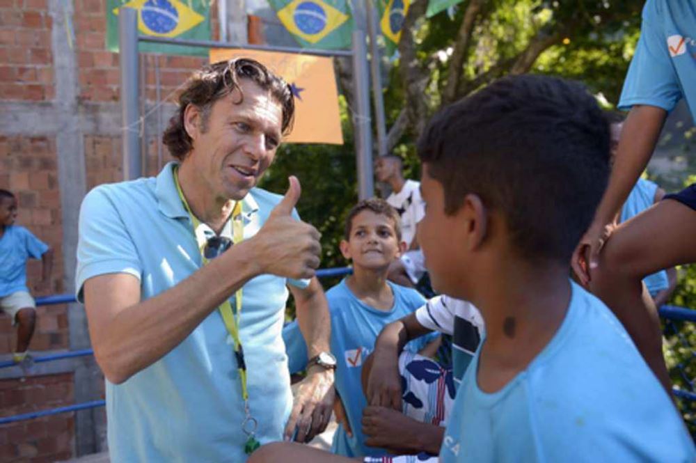 Urs Meier zeigt Daumen hoch zu einem Kind in Brasilien (Quelle: Kindernothilfe) Urs Meier zeigt hat eine Pfeife im Mund und zeigt eine rote Karte