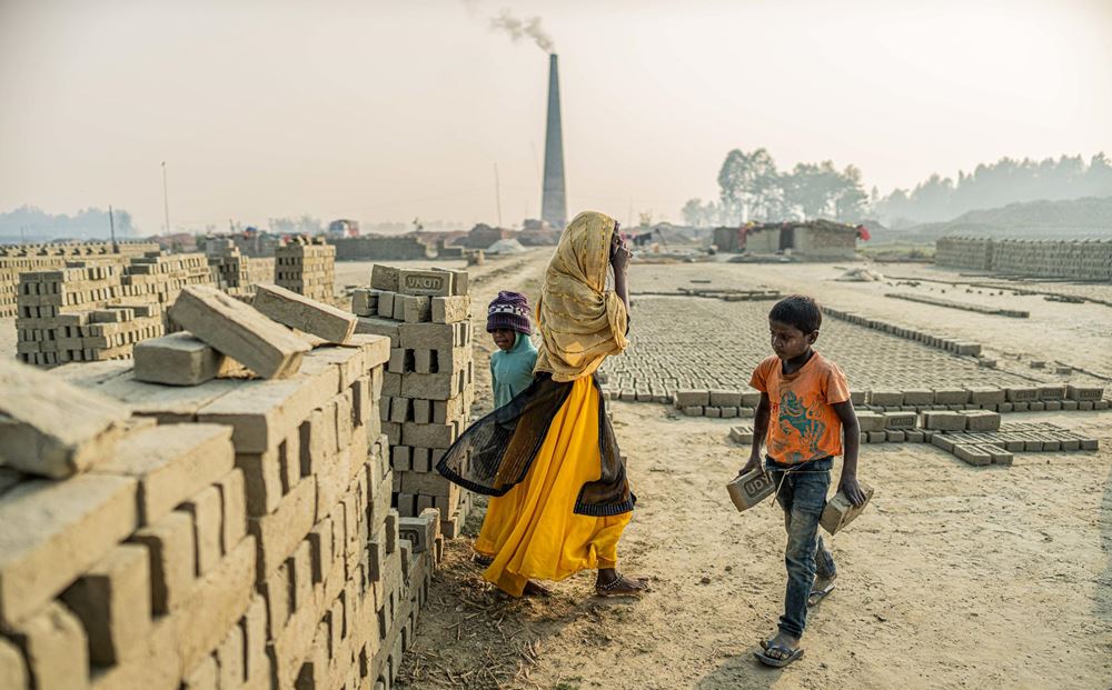 Kinder bestücken eine Mauer aus rohen Ziegeln mit neuen Ziegeln; im Hintergrund lagern Hunderte von Ziegeln zum Trocknen in der Sonne, am Ende des Geländes qualmt ein Schornstein (Quelle: Jakob Studnar) Kinder bestücken eine Mauer aus rohen Ziegeln mit neuen Ziegeln; im Hintergrund lagern Hunderte von Ziegeln zum Trocknen in der Sonne, am Ende des Geländes qualmt ein Schornstein (Quelle: Jakob Studnar)