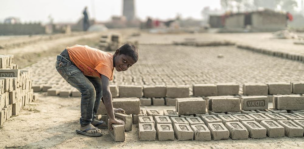 Eine große Fläche mit Ziegeln, die zum Trocknen in der Sonne liegen - ein Junge hebt zwei von ihnen auf (Quelle: Jakob Studnar) Eine große Fläche mit Ziegeln, die zum Trocknen in der Sonne liegen - ein Junge hebt zwei von ihnen auf (Quelle: Jakob Studnar)