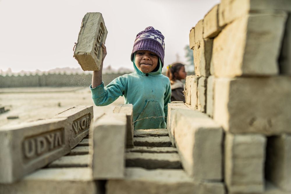 Ein kleines Kind wuchtet einen Ziegel auf eine Ziegelmauer (Quelle: Jakob Studnar) Ein kleines Kind wuchtet einen Ziegel auf eine Ziegelmauer (Quelle: Jakob Studnar)