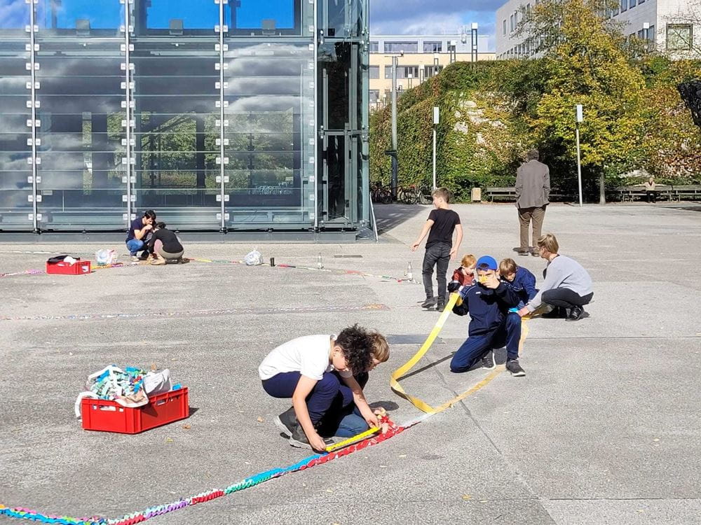 Schüler legen Papierschlangen auf einen großen Platz (Quelle: privat) Schüler legen Papierschlangen auf einen großen Platz (Quelle: privat)