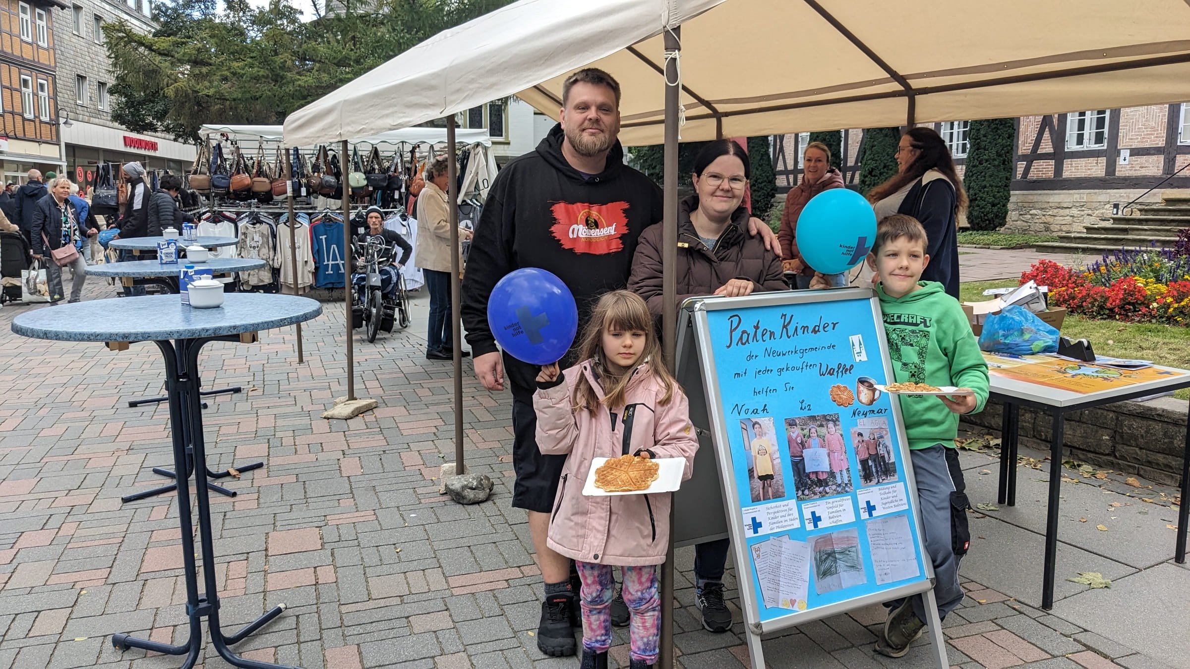 Ein Waffelstand, davor eine Familie mit einem selbst gemalten Plakat (Quelle: privat) Ein Waffelstand, davor eine Familie mit einem selbst gemalten Plakat (Quelle: privat)