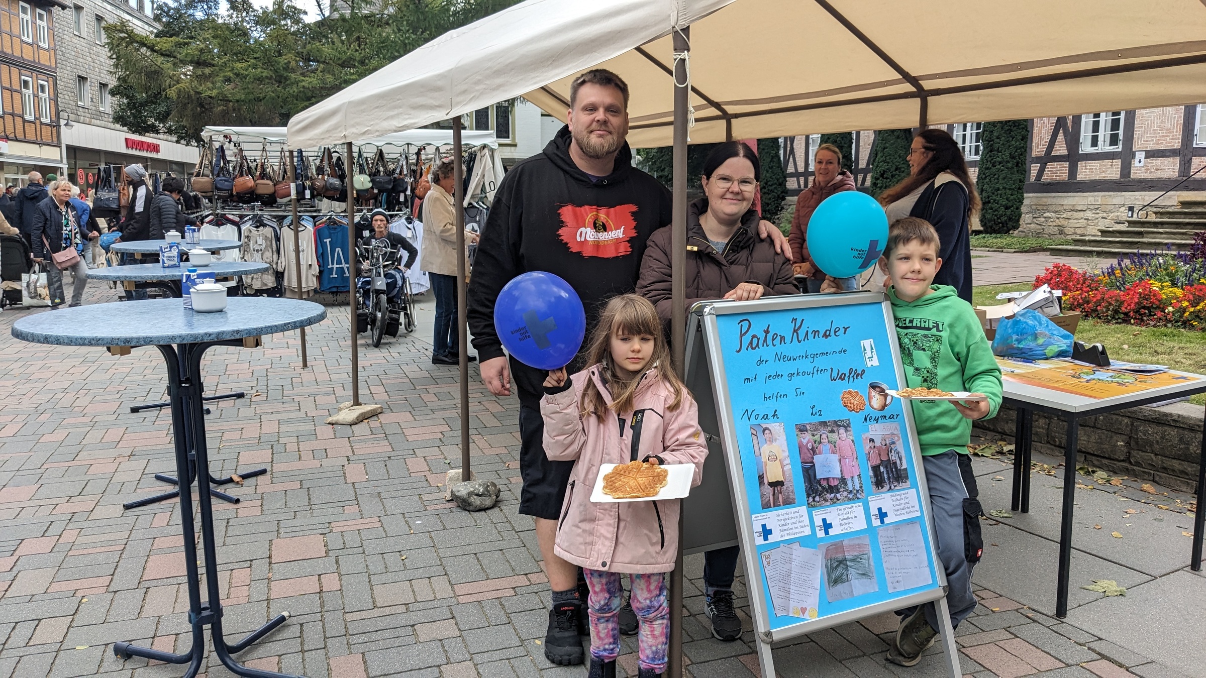 Ein Waffelstand, davor eine Familie mit einem selbst gemalten Plakat (Quelle: privat) Ein Waffelstand, davor eine Familie mit einem selbst gemalten Plakat (Quelle: privat)