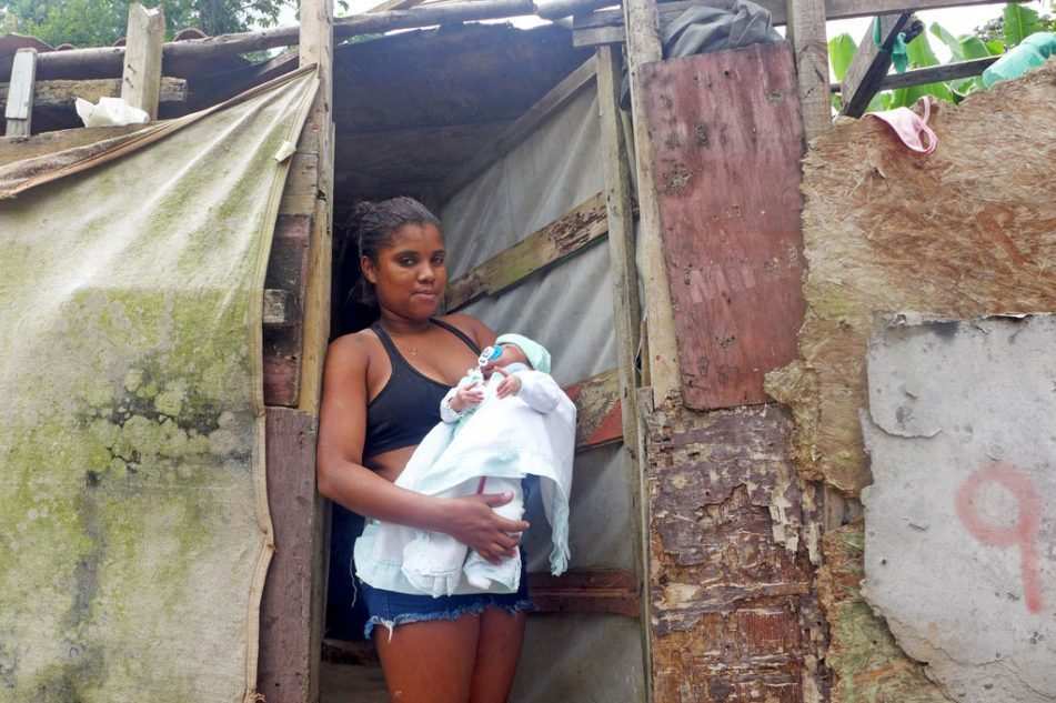 Eine junge Frau steht vor einer Hütte mit Baby auf dem Arm (Quelle: Kindernothilfe) Eine junge Frau steht vor einer Hütte mit Baby auf dem Arm (Quelle: Kindernothilfe)