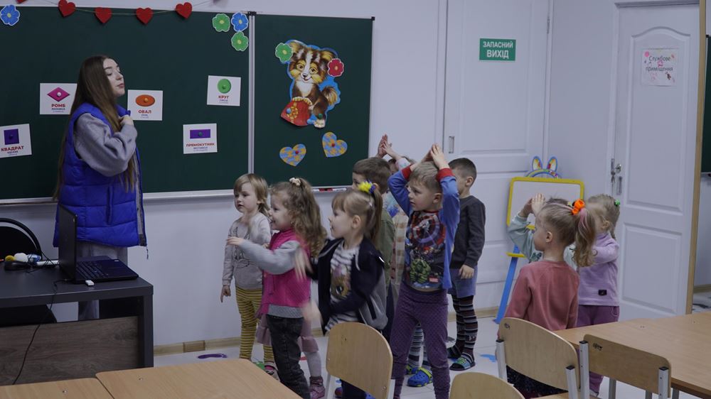 Eine Lehrerin und eine Gruppe von Kindern stehen vor einer Tafel (Quelle: Myrne Nebo) Eine Lehrerin und eine Gruppe von Kindern stehen vor einer Tafel (Quelle: Myrne Nebo)