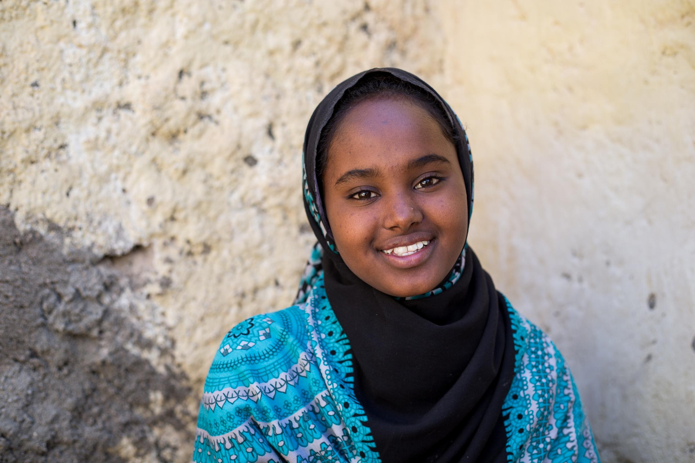 Ein Mädchen aus Somaliland sitzt lächelnd vor einer Mauer. (Quelle: Mustafa Saeed)