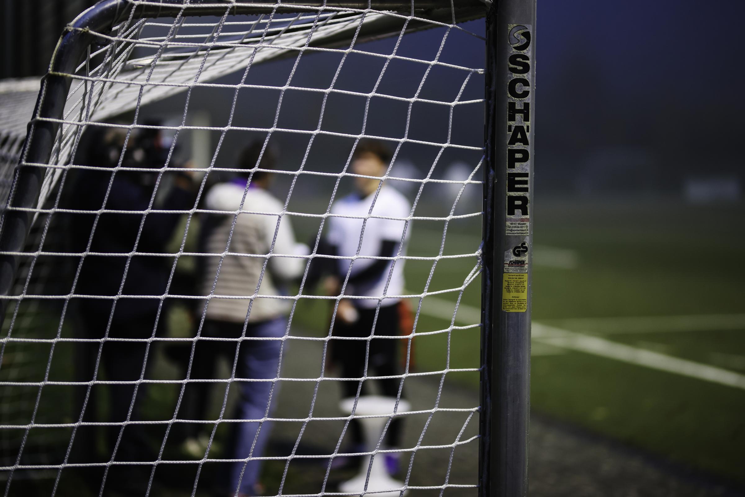 Auf dem Bild ist ein Sportplatz zu sehen, auf dem ein Fußballtor steht. Unscharf dahinter sind Jugendliche, die sich unterhalten. Foto: Martin Bondzio/Kindernothilfe