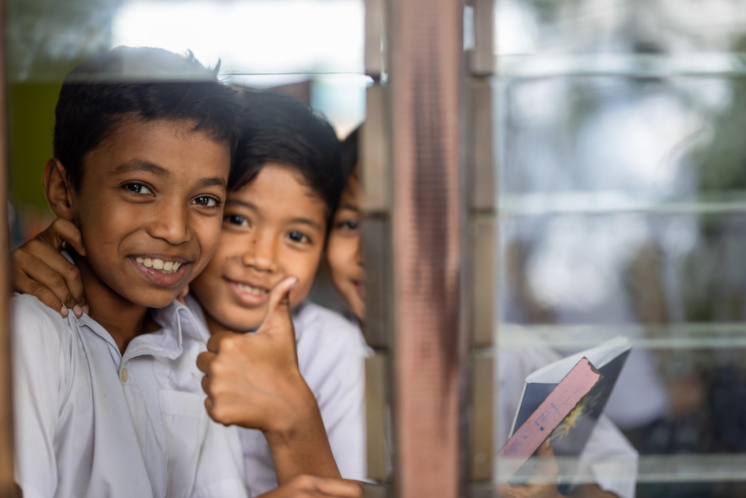 Geflüchtete Jungen aus Myanmar blicken fröhlich durch ein Schulfenster (Quelle: Lars Heidrich)