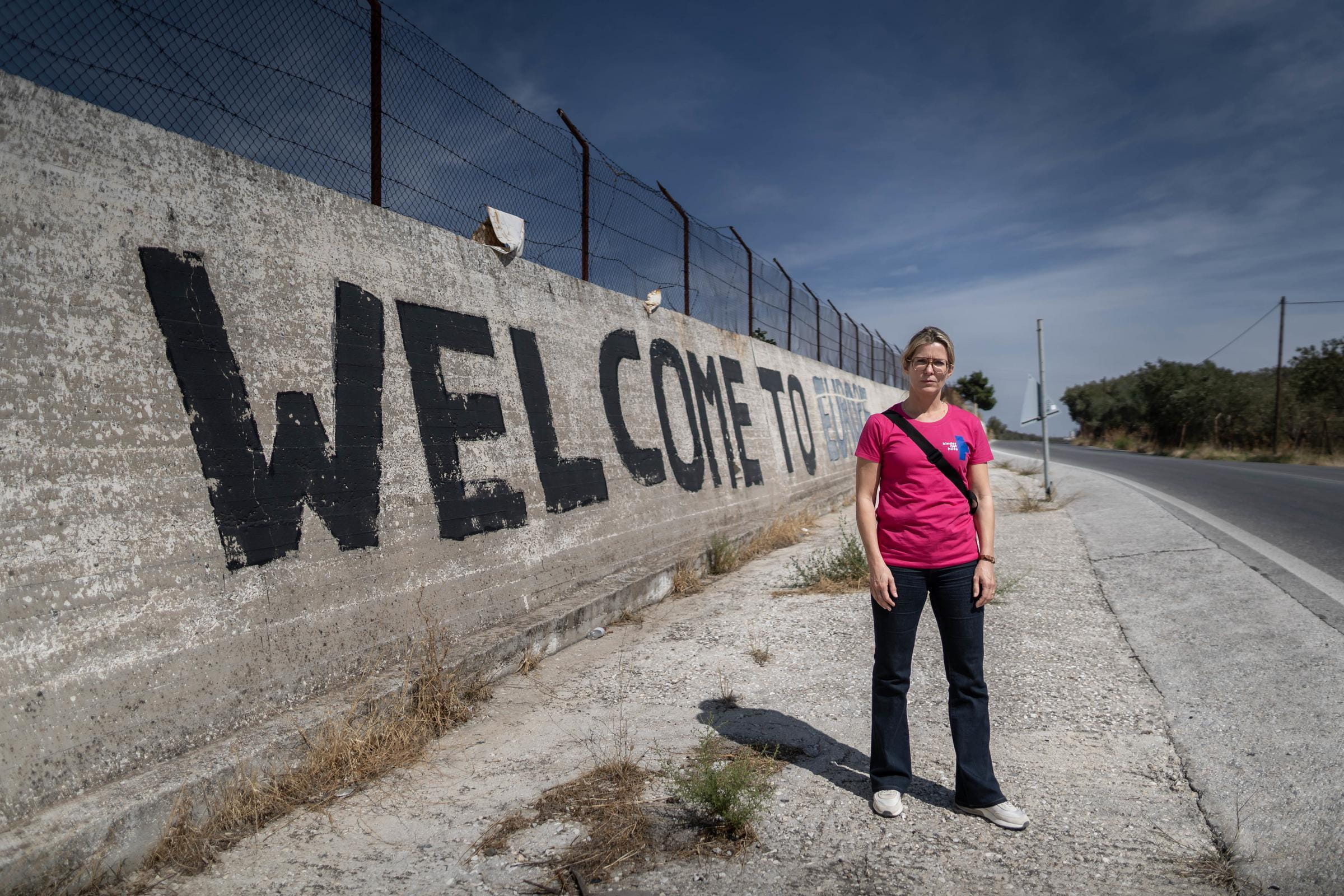 Eine Frau im pinkfarbenen Kindernothilfe-Shirt steht vor einer Mauer mit dem Schriftzug Welcome to Europe (Quelle: Lars Heidrich)