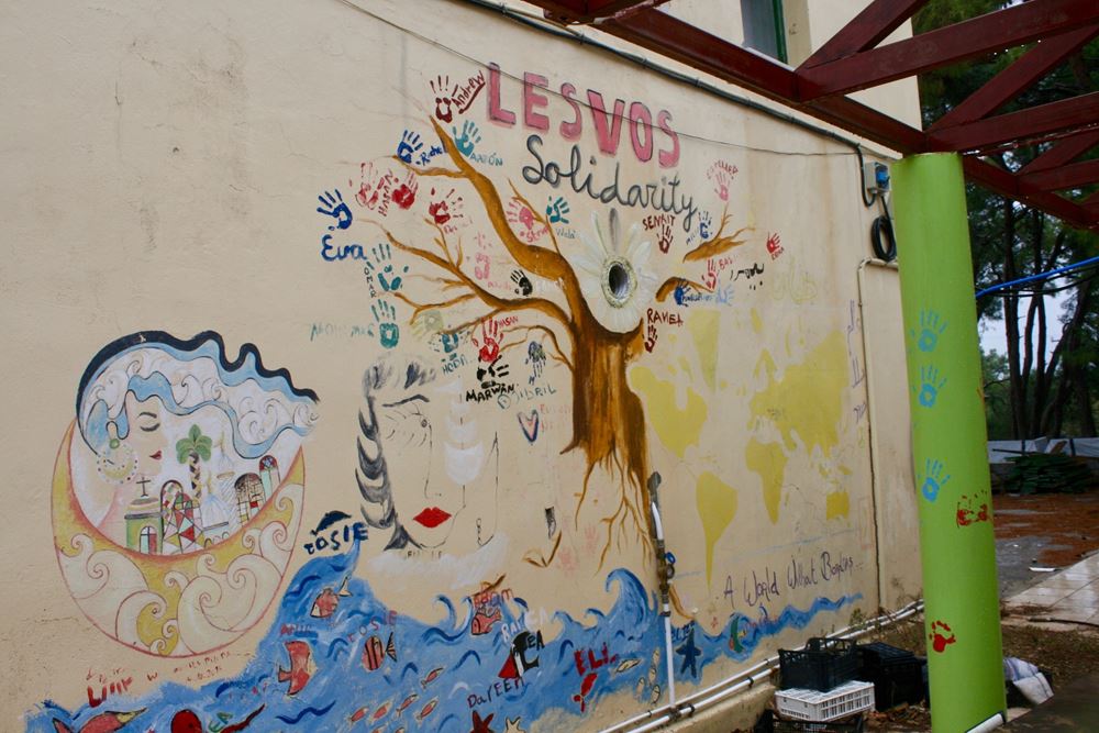 Wandbild: Ein Baum mit bunten Handabdrücken und Namen anstelle von Blättern, darübre steht Lesvos Soildarity (Quelle: Jürgen Schübelin) Wandbild: Ein Baum mit bunten Handabdrücken und Namen anstelle von Blättern, darübre steht Lesvos Soildarity (Quelle: Jürgen Schübelin)
