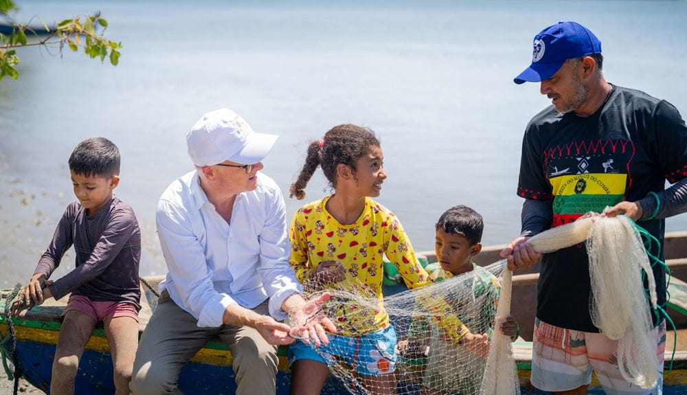 Karsten Schwanke, Kindernothilfe-Botschafter, lässt sich von den Einwohner*innen mehr über die Folgen des Klimawandels erklären und hält dabei ein Fischernetz in der Hand. Foto: Jakob Studnar Platzhalterbild