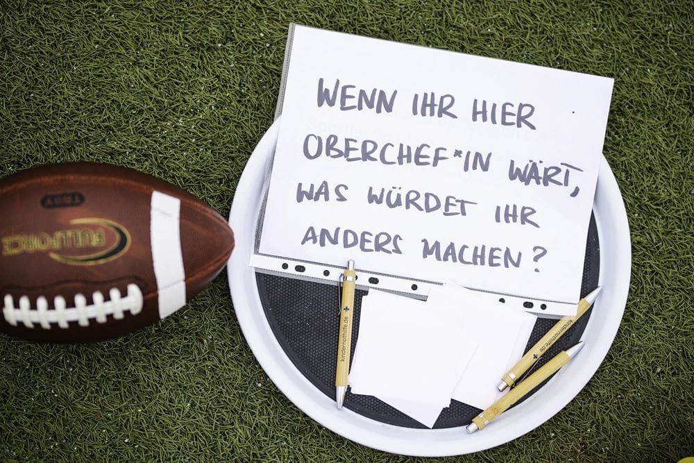 Schild, Zettel und Stifte neben einem Football. Auf dem Schild steht: "Wenn ihr hier Oberchef*in wärt, was würdet ihr anders machen?" (Quelle: Kindernothilfe) Schild, Zettel und Stifte neben einem Football. Auf dem Schild steht: "Wenn ihr hier Oberchef*in wärt, was würdet ihr anders machen?" (Quelle: Kindernothilfe)