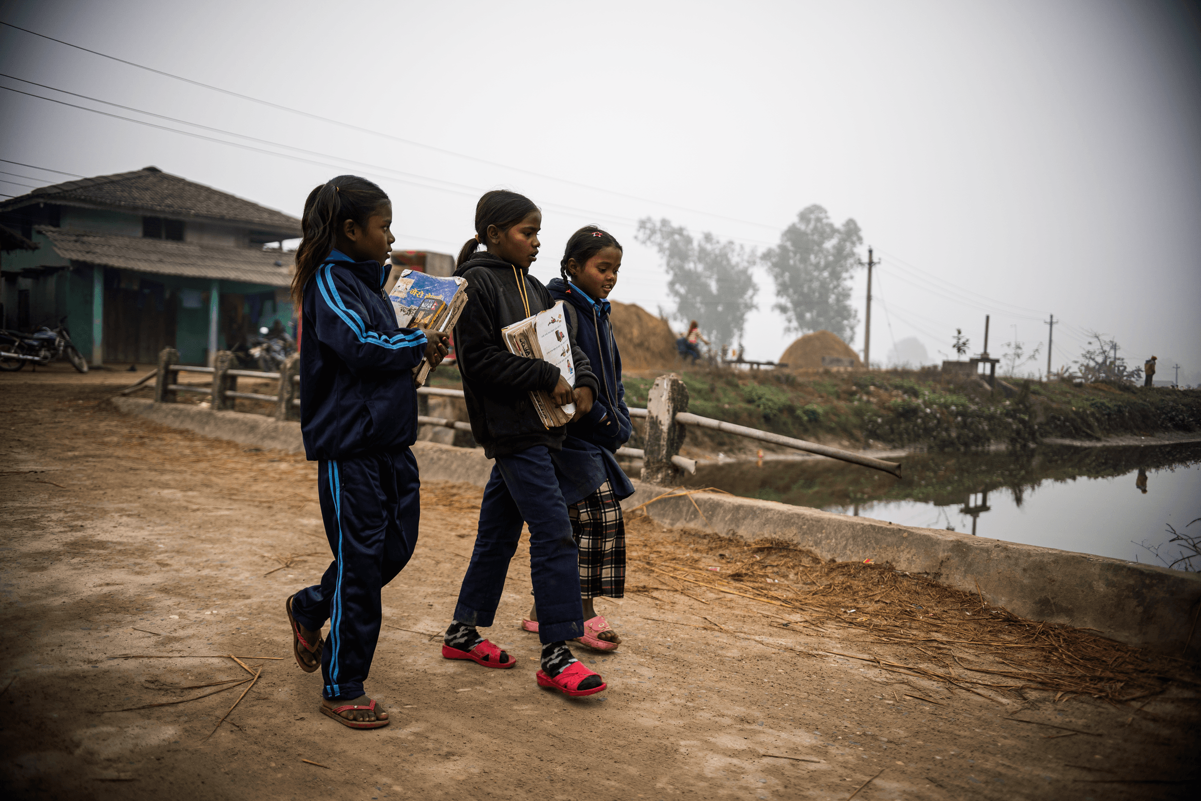 Drei nepalesische Mädchen laufen auf einem Weg über einen Fluss (Quelle: Martin Bondzio/Kindernothilfe)