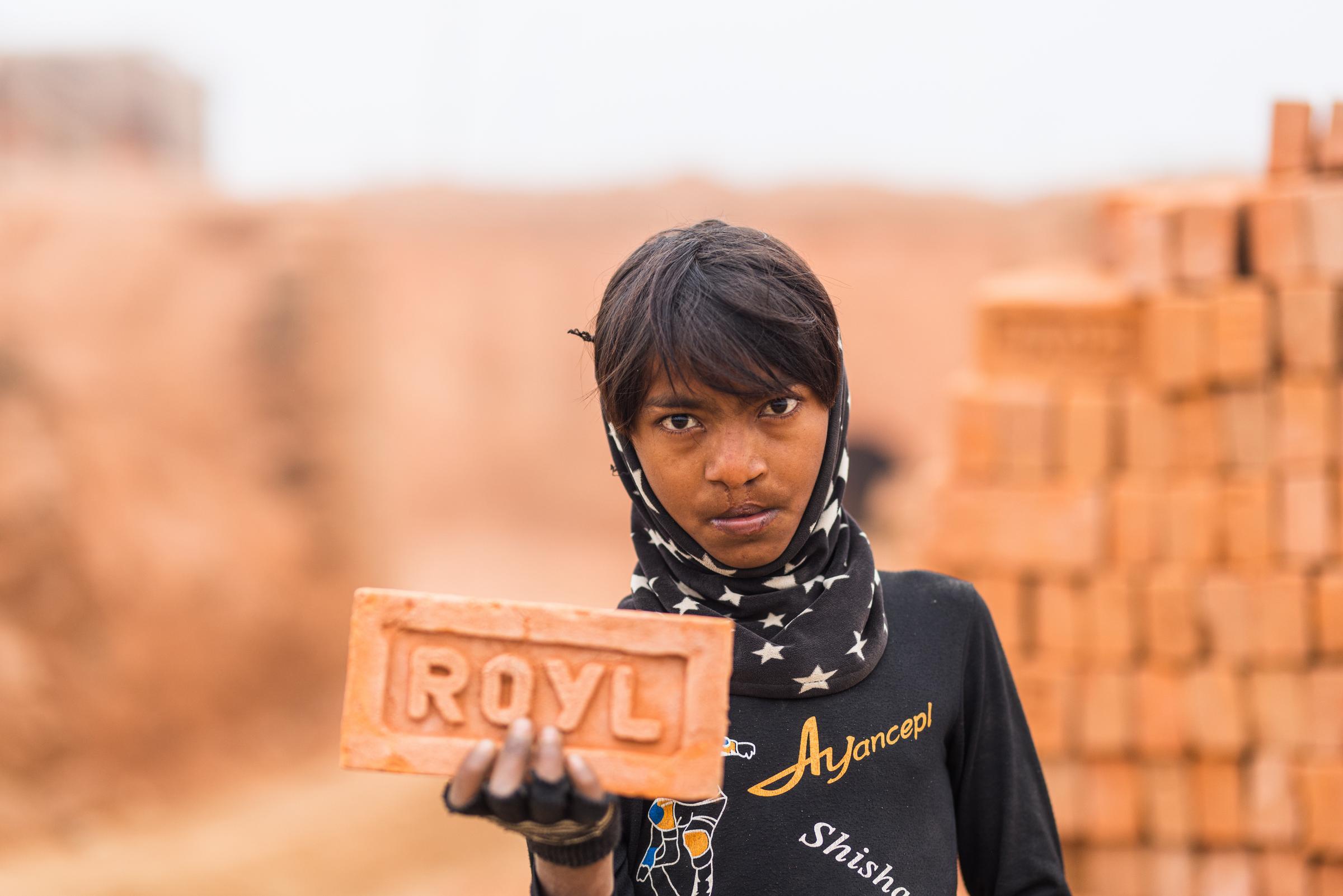 Ein Junge, der in einer Ziegelei arbeiten muss, hält einen schweren Ziegelstein in die Kamera (Foto: Martin Bondzio/Kindernothilfe)
