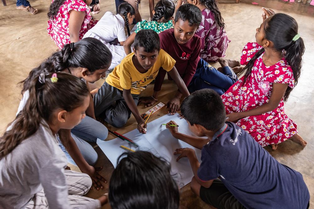 Kinder aus Sri Lanka sitzen in einem Kreis auf dem Boden und gestalten gemeinsam ein Plakat (Quelle: Sharni Jayawardena/Kindernothilfe) Kinder aus Sri Lanka sitzen in einem Kreis auf dem Boden und gestalten gemeinsam ein Plakat (Quelle: Sharni Jayawardena/Kindernothilfe)