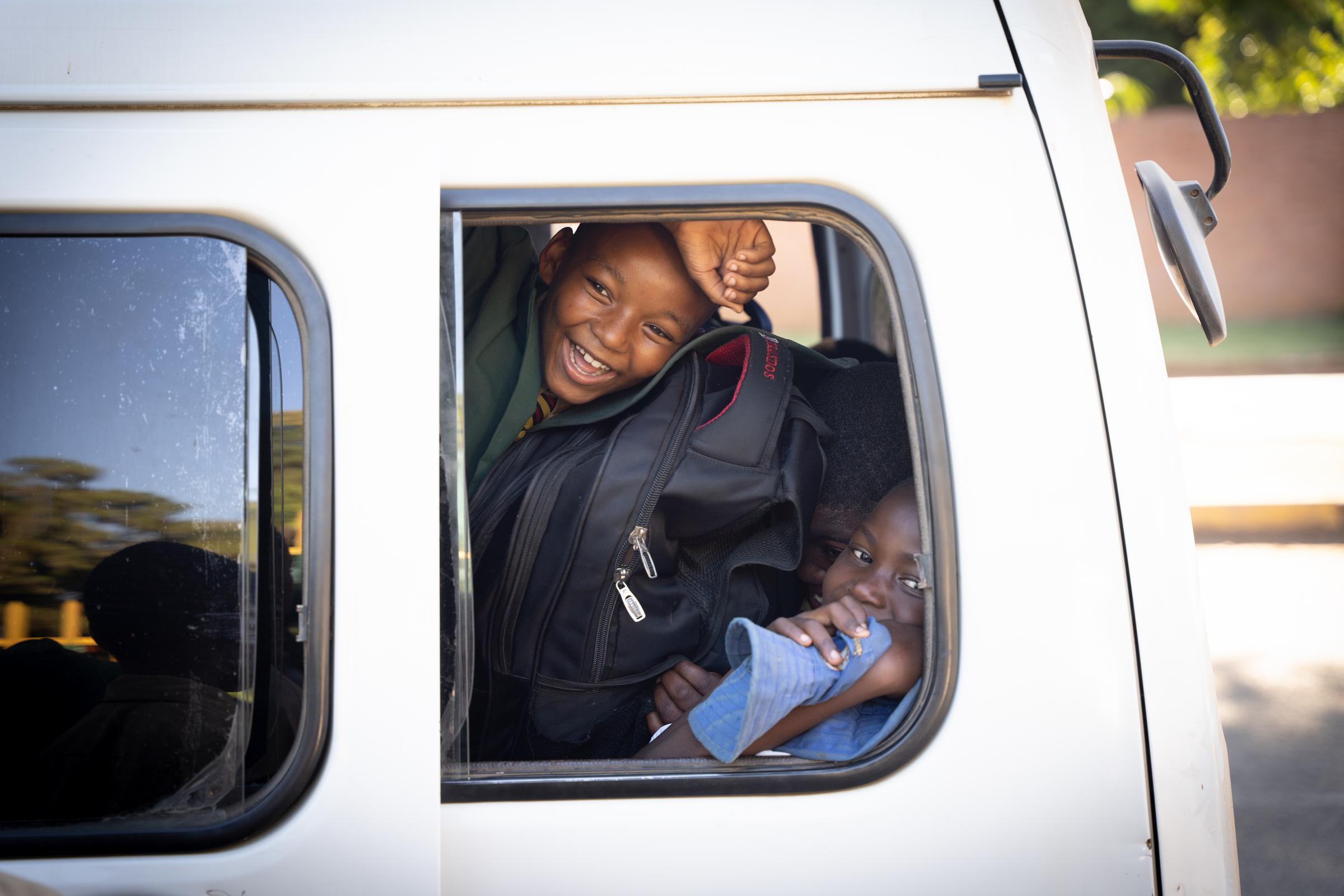 Schüler schauen lachend aus dem Fenster eines Schulbusses, der sie sicher zur Schule bringt (Foto: Christian Nusch)