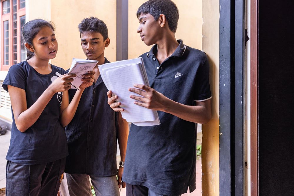 Drei Jugendliche aus dem Theaterworkshop stehen zusammen und schauen auf ihre auf Zettel aufgeschriebenen Gedanken. "Keiner sieht mich an“ – mit den Worten des Baumes bringt Nadini zum Ausdruck, was sie selbst bewegt. Foto: Sharni Jayawardena Drei Jugendliche aus dem Theaterworkshop stehen zusammen und schauen auf ihre auf Zettel aufgeschriebenen Gedanken. "Keiner sieht mich an“ – mit den Worten des Baumes bringt Nadini zum Ausdruck, was sie selbst bewegt. Foto: Sharni Jayawardena