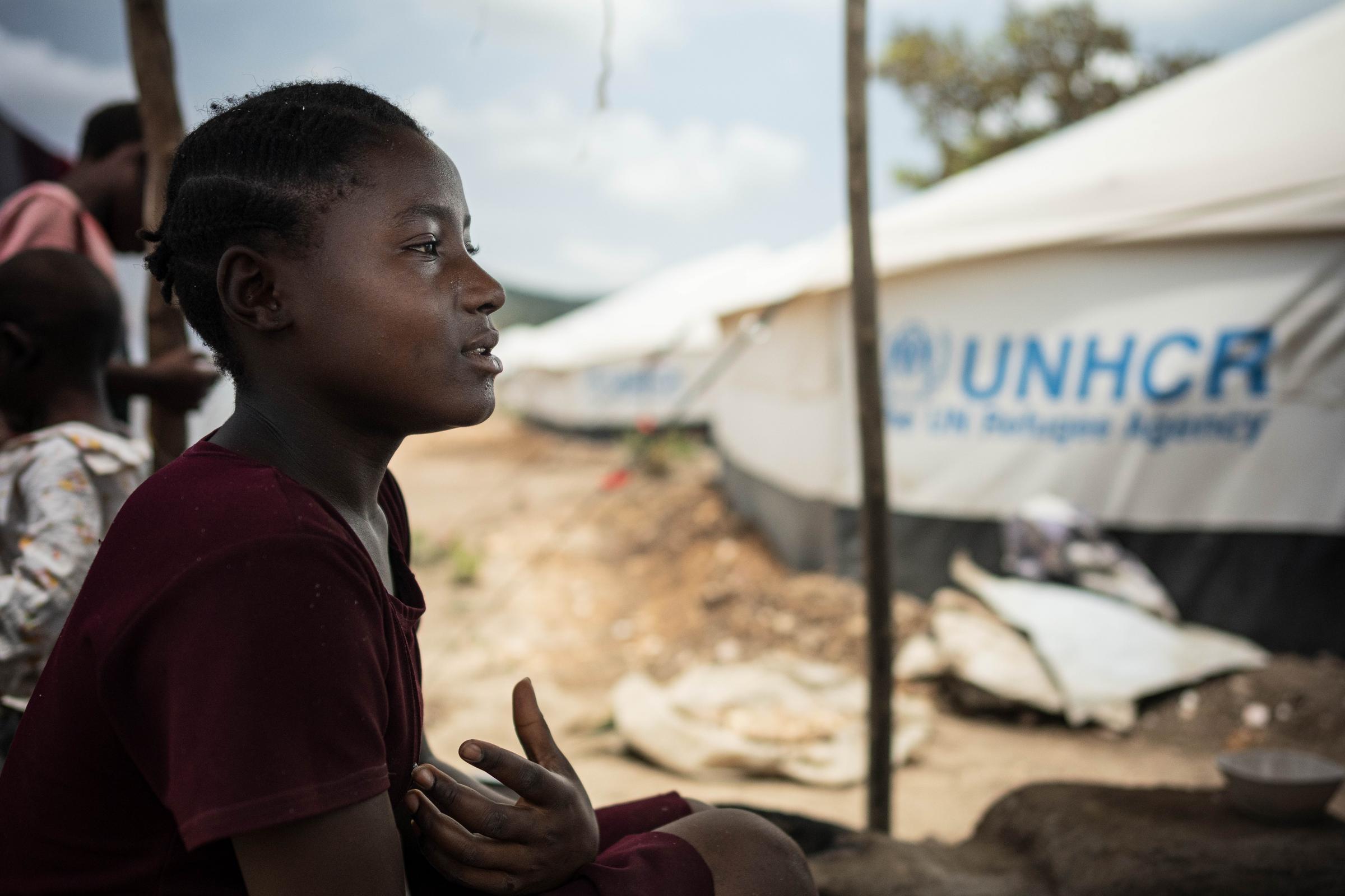 Bahati sitzt im Schatten, im Hintergrund sieht man ein Zelt (Quelle: Jakob Studnar)