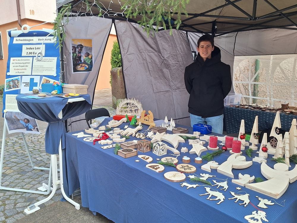 Weihnachtsmarktstand in Gaertingen - Simeon steht hinter dem Stand, auf dem seine kreativen Werke stehen, und schaut in die Kamera (Foto: privat) Weihnachtsmarktstand in Gaertingen - Simeon steht hinter dem Stand, auf dem seine kreativen Werke stehen, und schaut in die Kamera (Foto: privat)