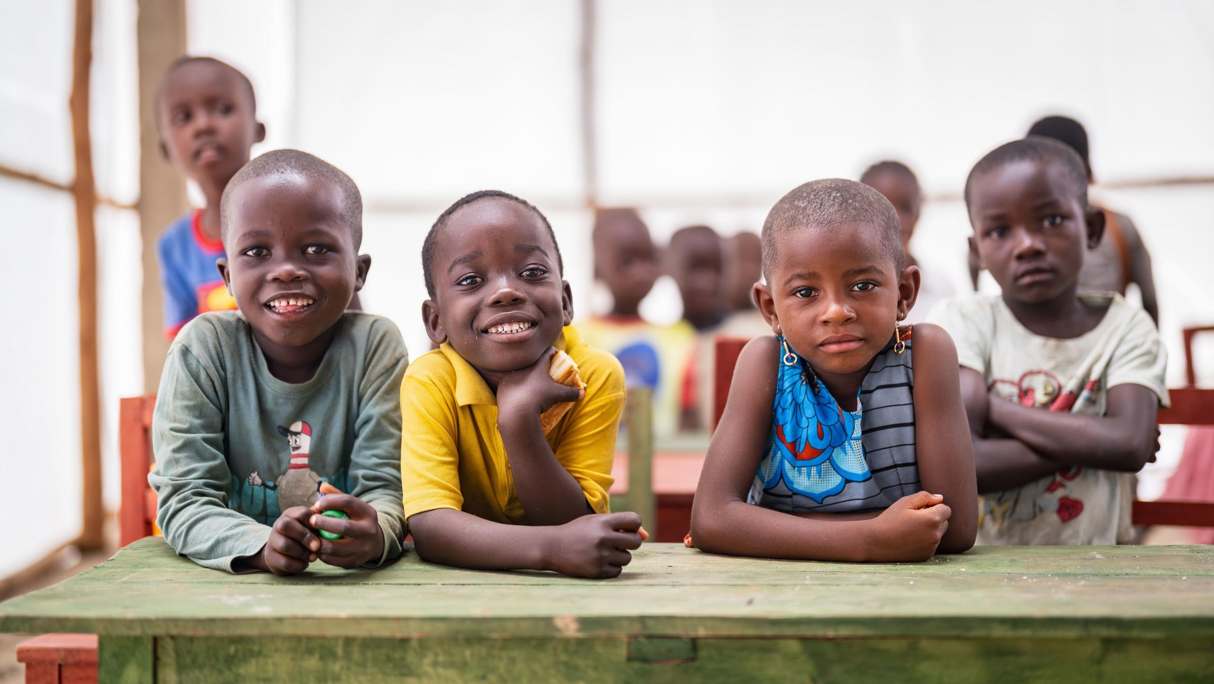Lächelnde Kinder sitzen an einem Tisch im Kindergartenzelt im Flüchtlingslager Musenyi in Burundi (Quelle: Jakob Studnar) Lächelnde Kinder sitzen an einem Tisch im Kindergartenzelt im Flüchtlingslager Musenyi in Burundi (Quelle: Jakob Studnar)