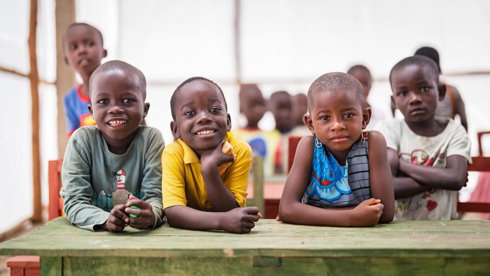 Lächelnde Kinder sitzen an einem Tisch im Kindergartenzelt im Flüchtlingslager Musenyi in Burundi Platzhalterbild