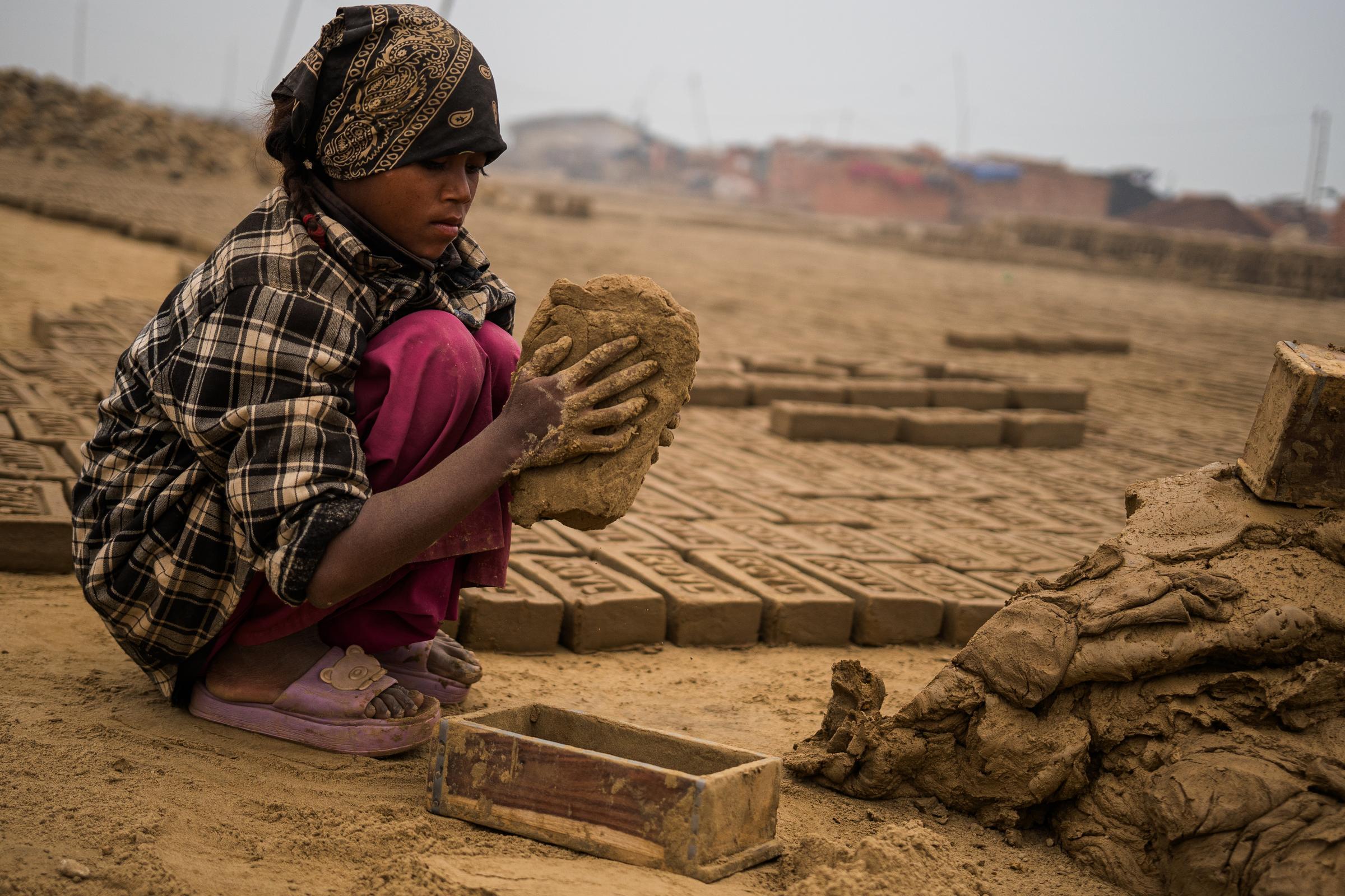 Ein Mädchen formt schwere Ziegel aus Ton auf dem Gelände einer Ziegelei in Nepal (Quelle: Martin Bondzio)