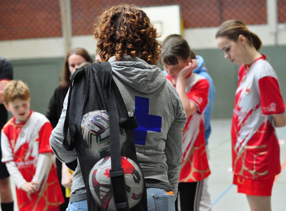 Eine Kindernothilfe-Mitarbeiterin steht mit Jugendlichen in einer Sporthalle. Die Mitarbeiterin trägt in einer Tasche zwei Fußbälle. (Quelle: Friederike Bach) Eine Kindernothilfe-Mitarbeiterin steht mit Jugendlichen in einer Sporthalle. Die Mitarbeiterin trägt in einer Tasche zwei Fußbälle. (Quelle: Friederike Bach)