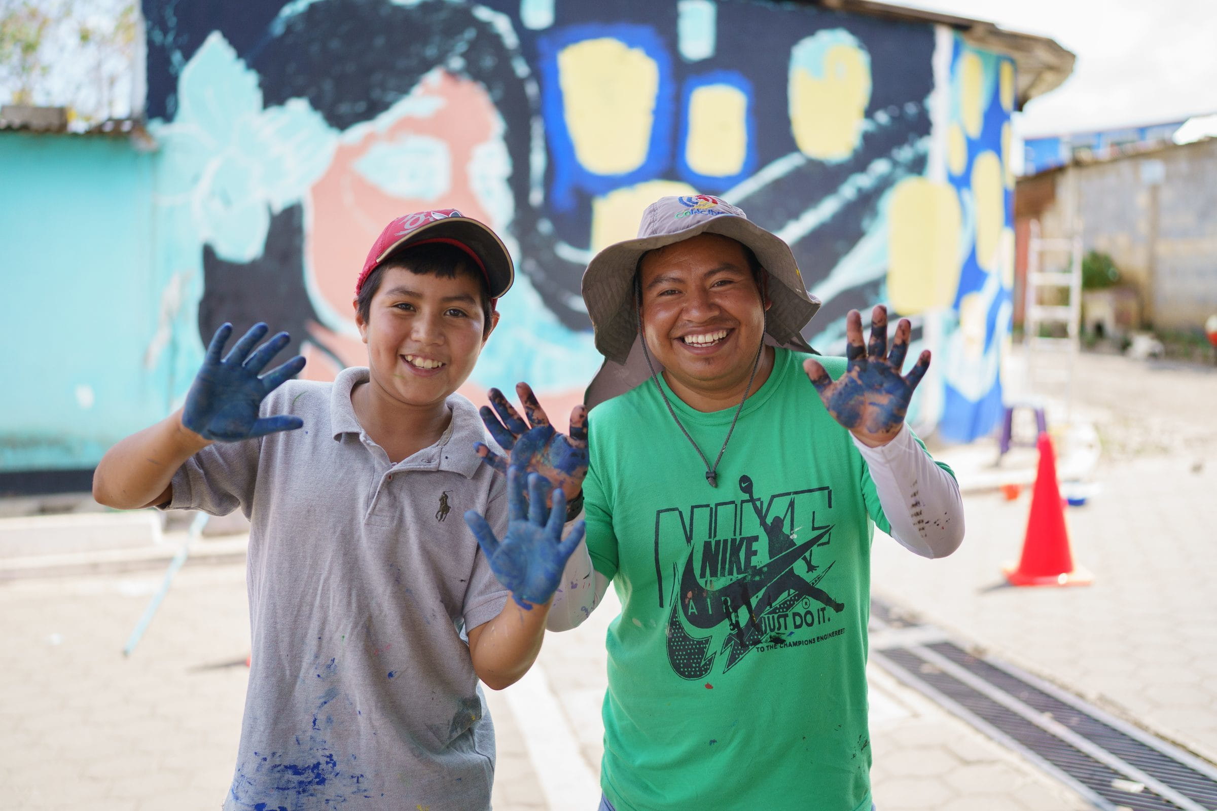 COINCIDIR Erzieher und ein Junge mit bunten Händen vor einem Wandbild (Quelle: James Rodríguez)