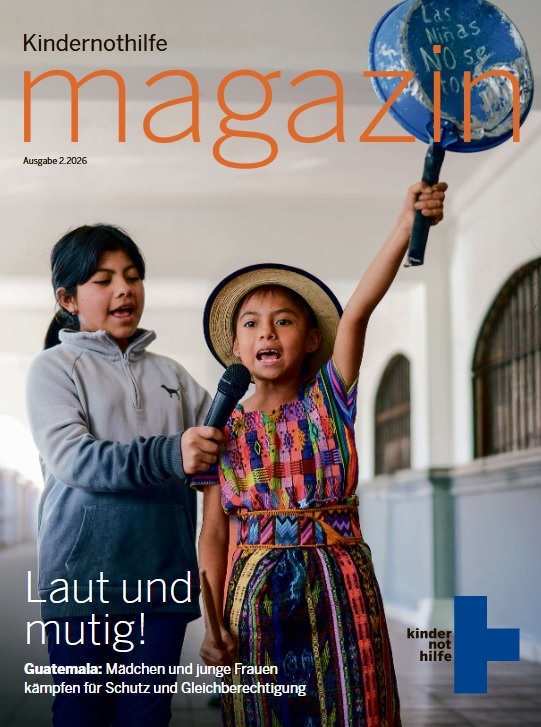 Magazin 2/2026 Titel Ein Mädchen hält eine Bratpfanne nach oben und spricht in ein Mikrofon, das ein anderes Mädchen neben ihr in der Hand hält 