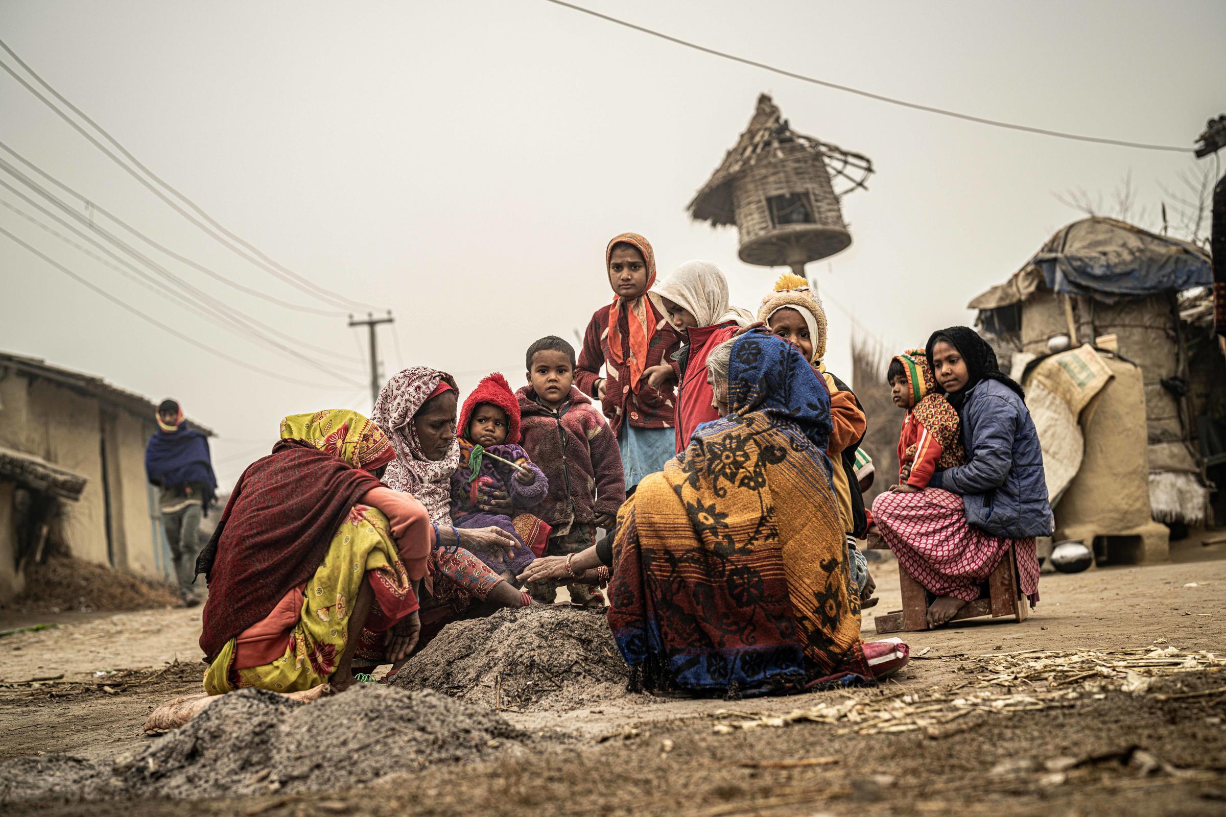 Eine größere Familie in Nepal sitzt draußen vor ihren Hütten auf dem Boden. Ein paar Kinder schauen in die Kamera. (Quelle: Jakob Studnar / Kindernothilfe)