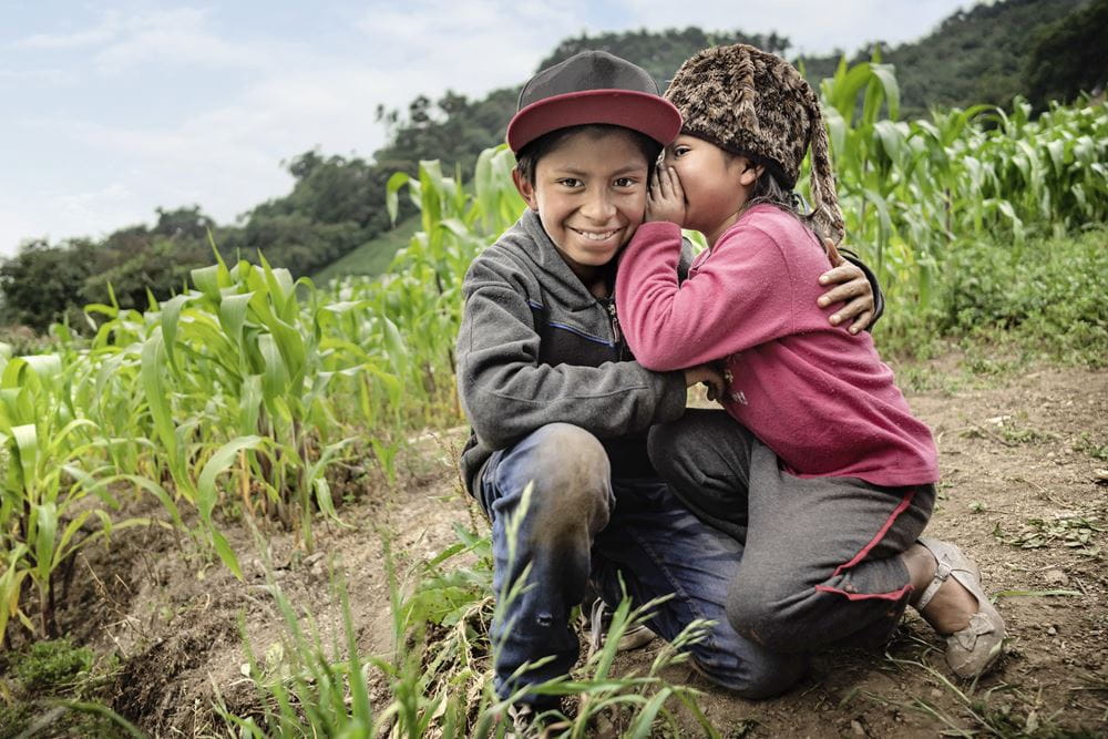 Mädchen flüstert ihrem Bruder auf einem Feld etwas ins Ohr. Guatemala (Quelle: Jakob Studnar)