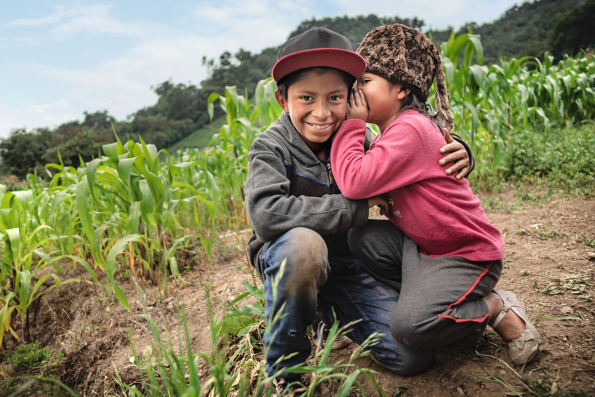 Mädchen flüstert ihrem Bruder auf einem Feld etwas ins Ohr. Guatemala (Quelle: Jakob Studnar)