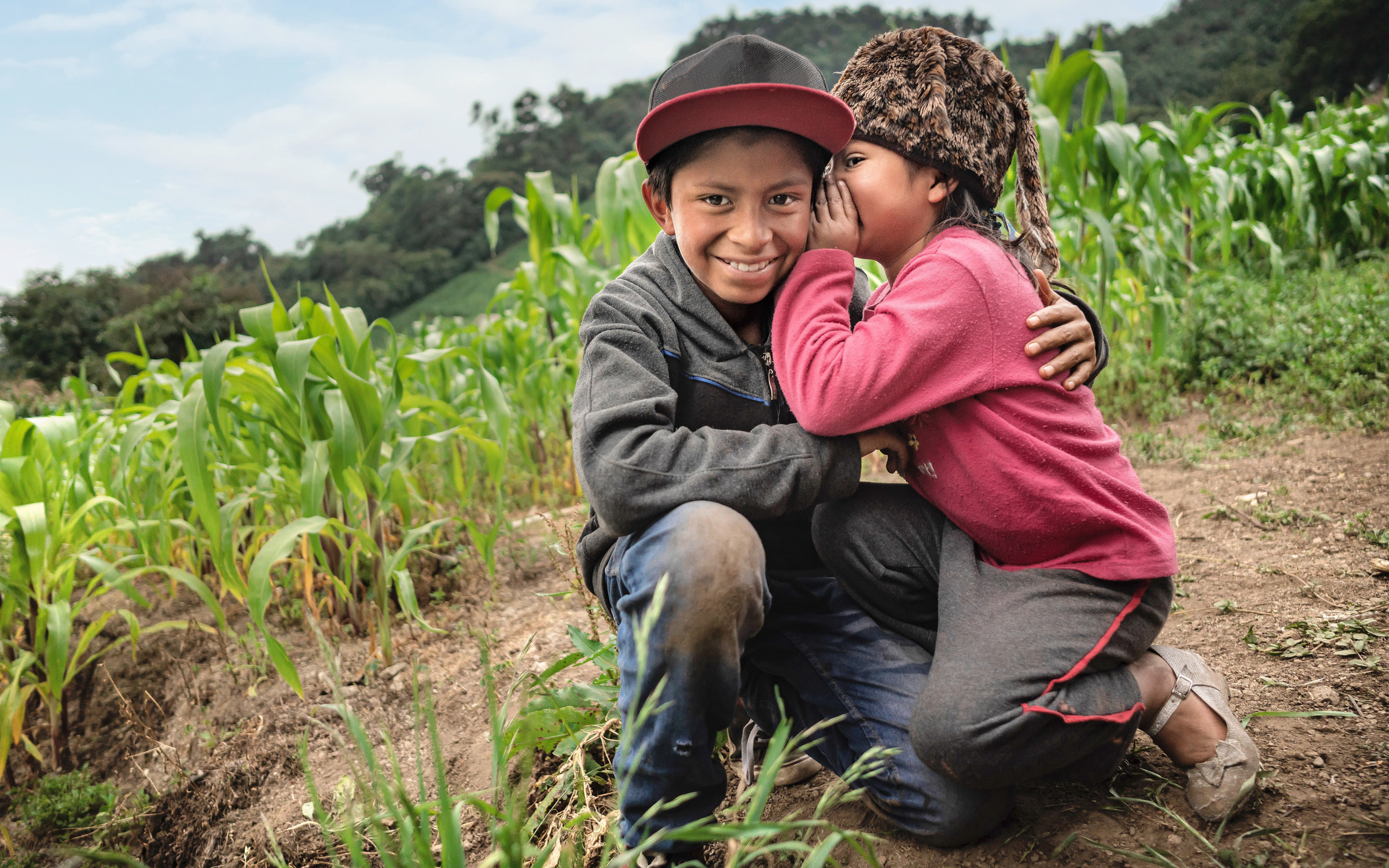 Mädchen flüstert ihrem Bruder auf einem Feld etwas ins Ohr. Guatemala (Quelle: Jakob Studnar)