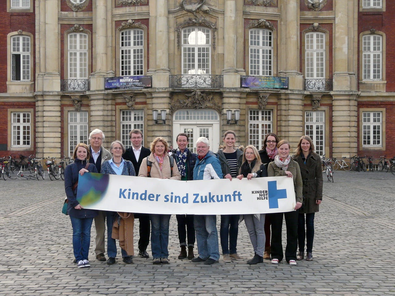 Gruppenfoto des Arbeitskreises Münster mit einem Kinder sind Zukunft Banner.  Gruppenfoto des Arbeitskreises Münster mit einem Kinder sind Zukunft Banner.