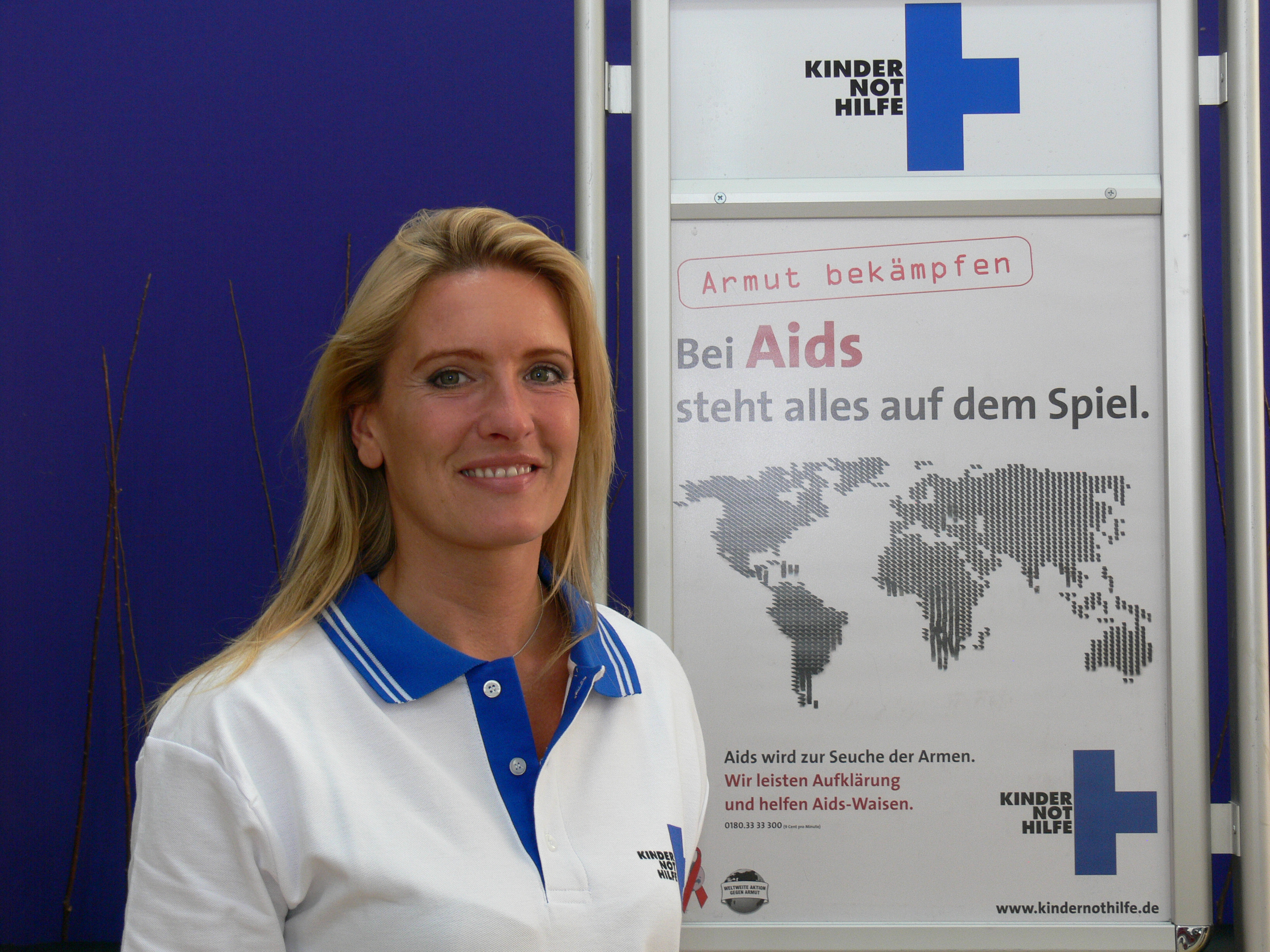 Claudia Kleinert auf dem Innenhafenfest in Duisburg vor einem Plakat zur AIDS-Aufklärung