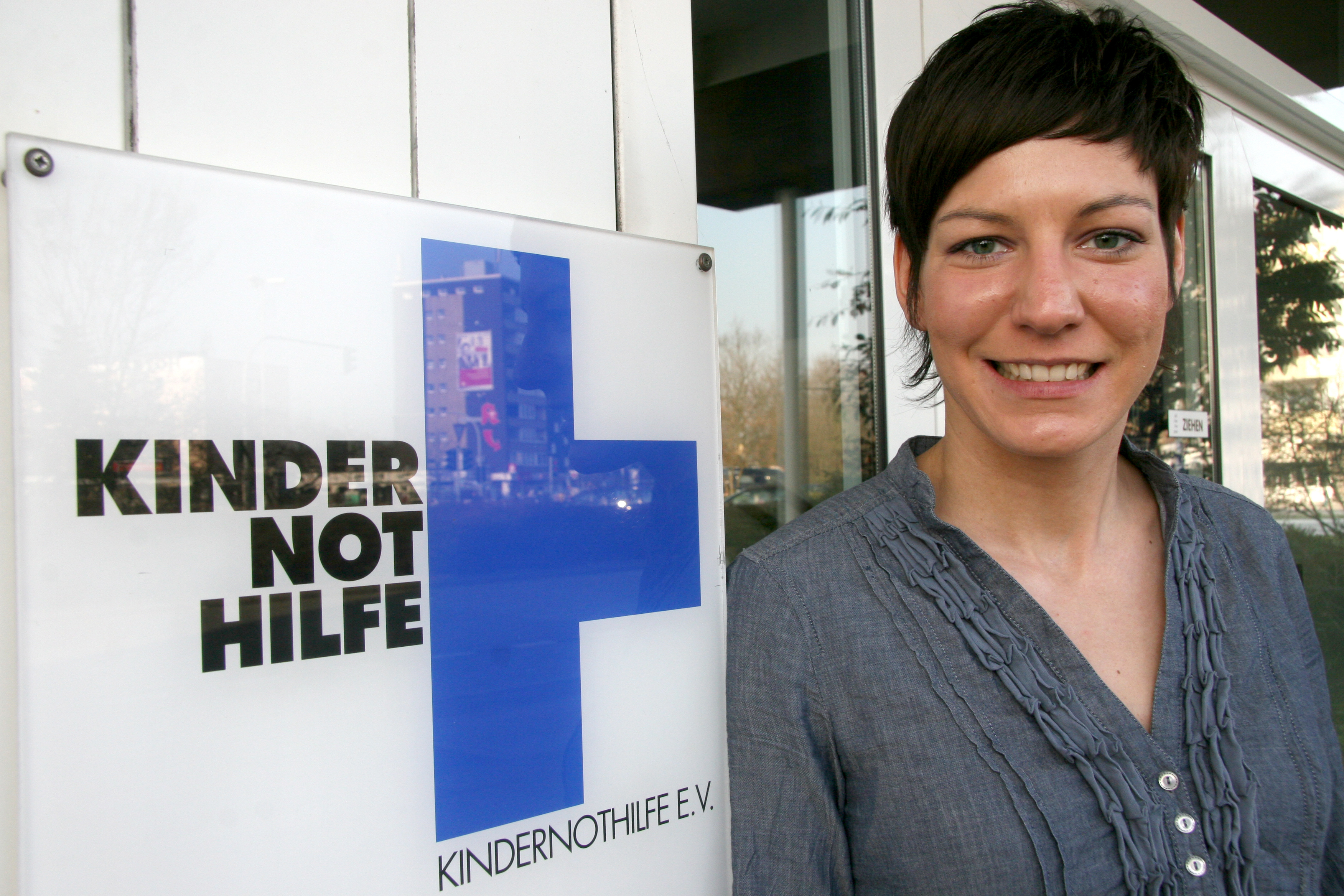 Linda Bresonik  lacht neben einem Kindernothilfe-Schild in die Kamera