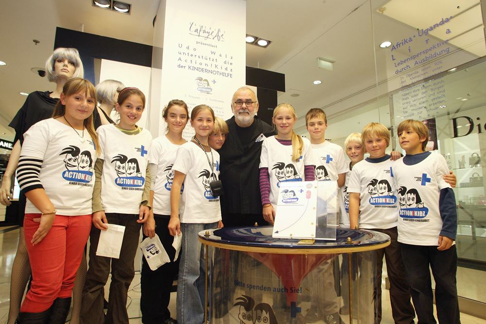 Udo Walz mit Kindern von der Action Kids Kampagne Udo Walz zeigt einem Kind an einer Puppe wie man Haare glättet