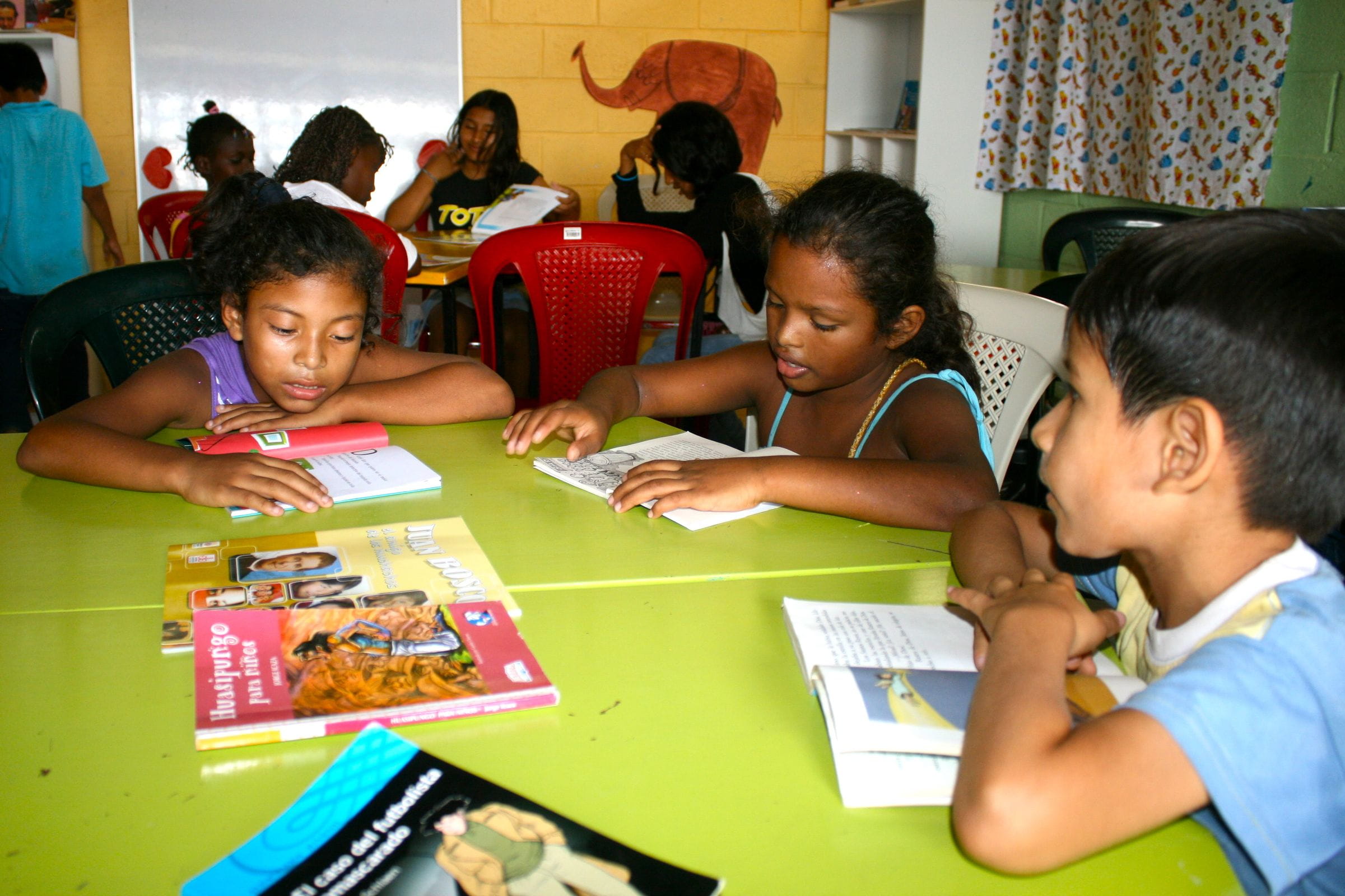 Kinder sitzen an einem bunten Tisch und lesen. (Quelle: Jürgen Schübelin)