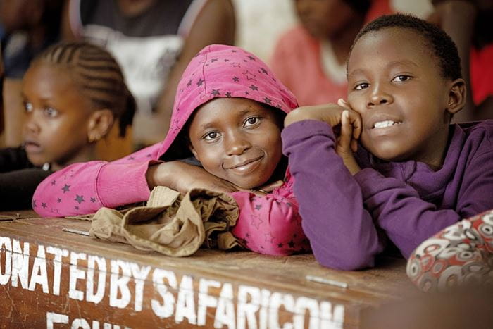 Kinder lehnen auf einer Schulbank und lächeln in die Kamera (Bild: Lars Heidrich)