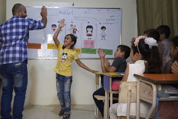 Ein Mädchen steht an der Tafel und klatscht lachend mit ihrem Lehrer ab. (Quelle: Ulrich Gernhardt)