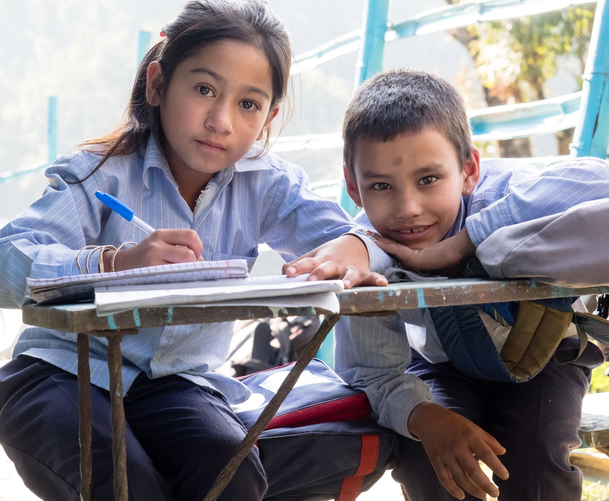 Ein Mädchen und ein Junge in hellblauer Schuluniform sitzen an einem Tisch und lachen. (Quelle: Steven Davies)