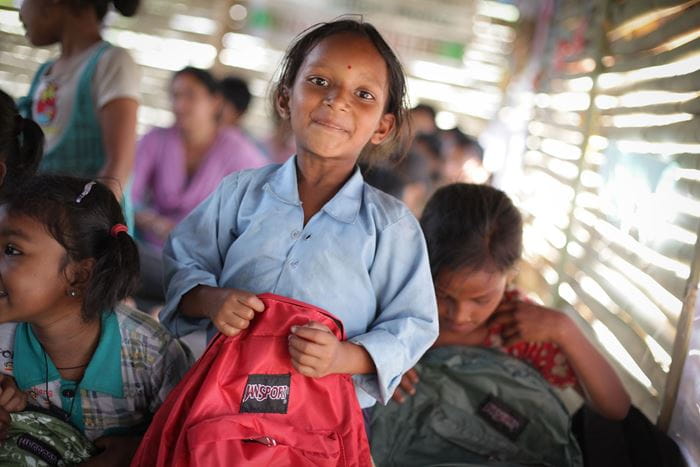 Ein Mädchen mit einem roten Rucksack in der Hand lacht. (Quelle: Bastian Strauch)