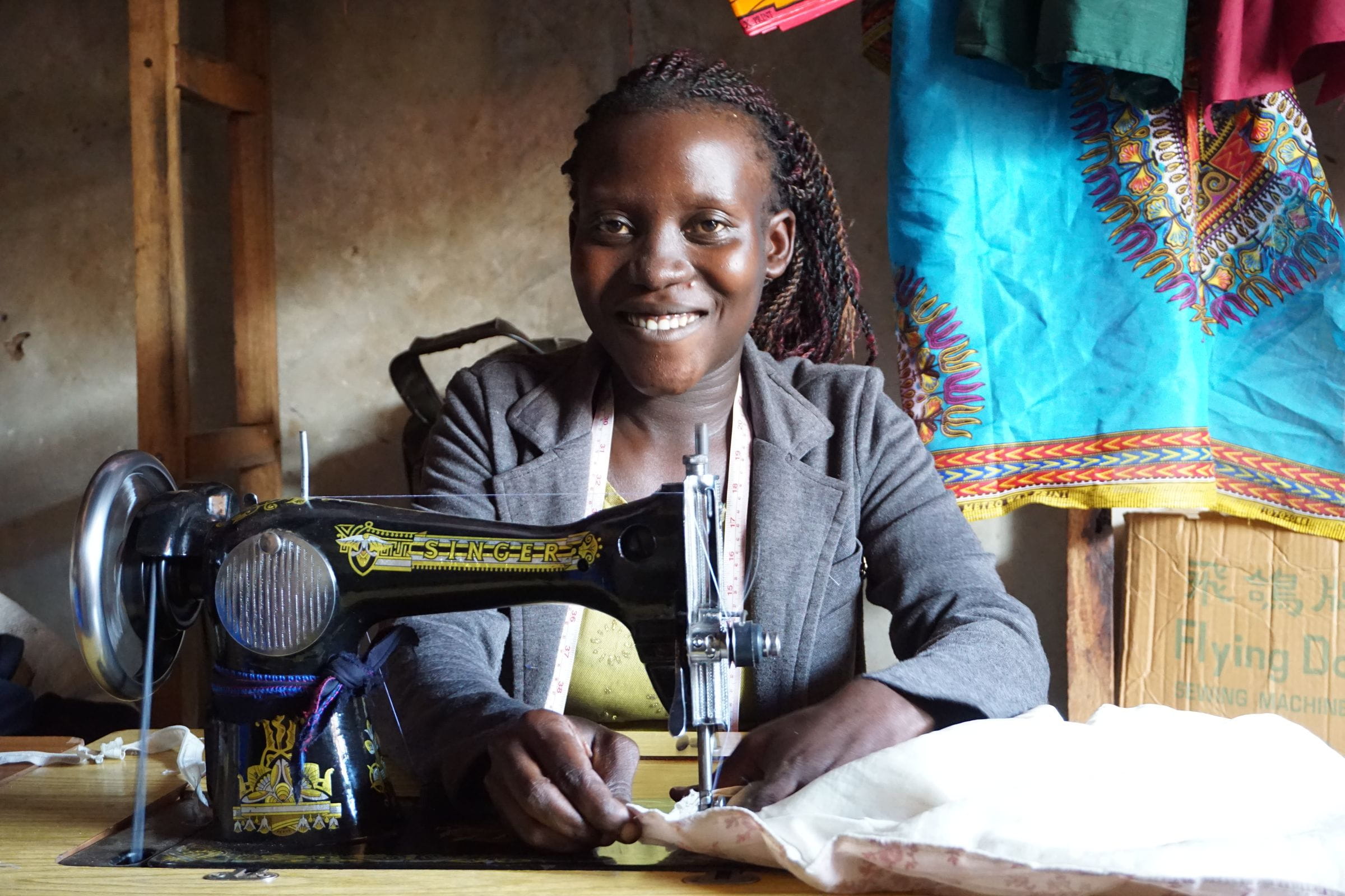 Eine Junge Frau sitzt lächelnd hinter ihrer Nähmaschine. (Quelle: Ludwig Grunewald)