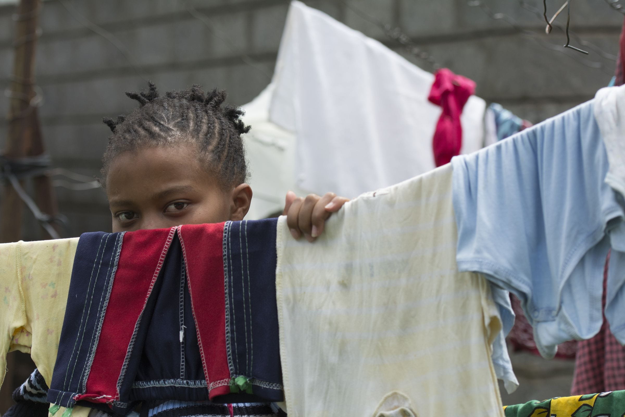 Auf einer Wäscheleine trocknet Wäsche. Diese verdeckt halb das Gesicht eines kenianischen Mädchens. (Quelle: Christian Nusch)