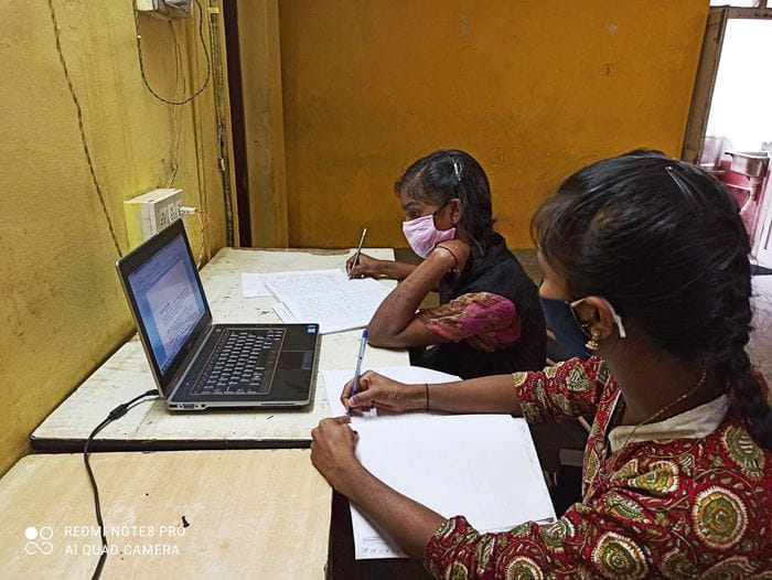 Zwei Mädchen in Indien sitzen vor eine Laptop und lauschen dem Online-Unterricht. (Quelle: Kindernothilfe-Partner)