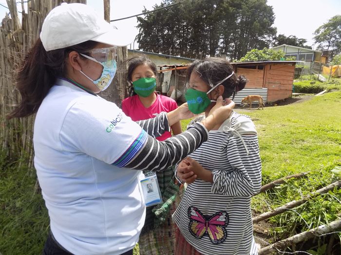 Mädchen in Guatemala erhalten einen Mund-Nasen-Schutz von einer Projektmitarbeiterin. (Quelle: Kindernothilfe-Partner)