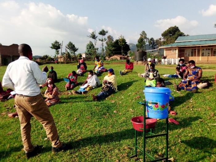 Eine Selbsthilfegruppe in Ruanda sitzt auf einer Wiese. Der mobile Handwaschapparat steht daneben. (Quelle: Kindernothilfe-Partner)