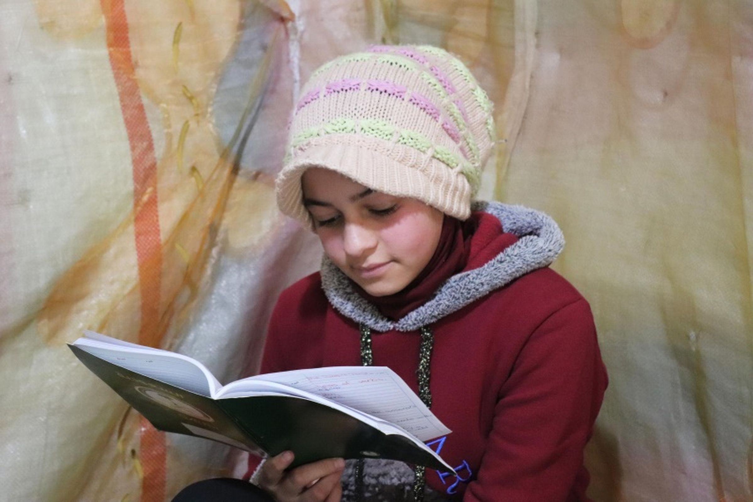 Ein syrisches Mädchen, dass nun in einem Flüchtlingscamp im Libanon lebt, sitzt im Zelt ihrer Familie und liest. (Quelle: ALPHA)