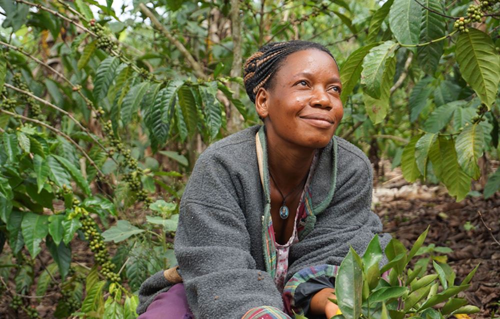 Eine Frau aus Uganda steht auf ihrem Feld und lächelt. (Quelle: Ludwig Grunewald)