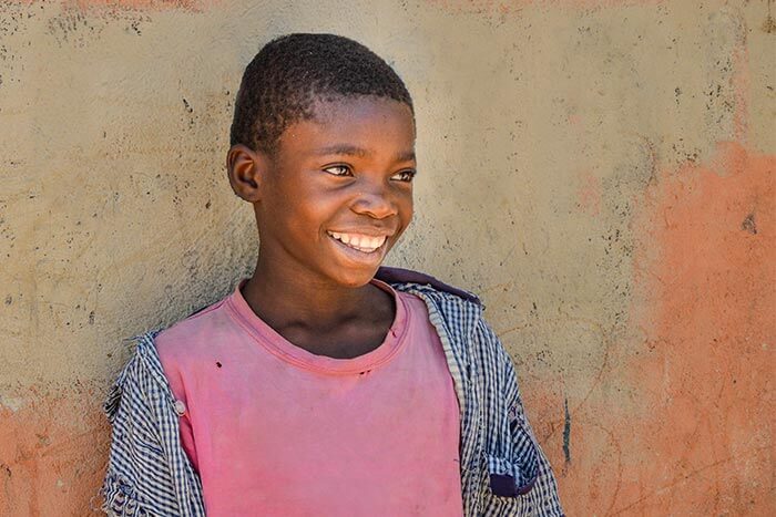 Ein Junge steht lächelnd an einer Wand.  (Quelle: Kindernothilfe)